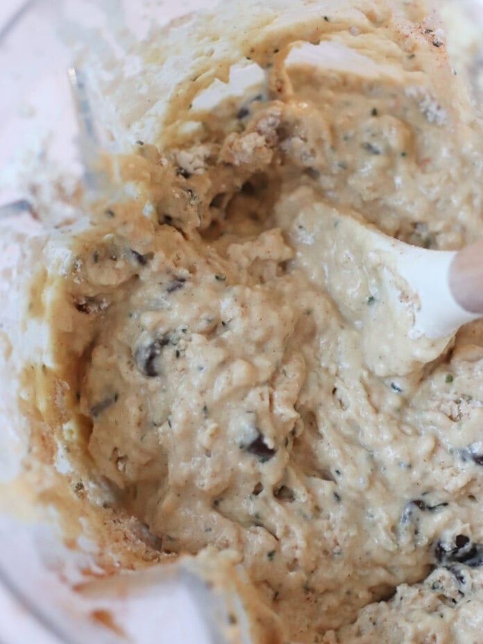 Close-up of thick, chunky cookie dough being mixed in a bowl with a white spatula. The dough contains chocolate chips and appears partially blended.