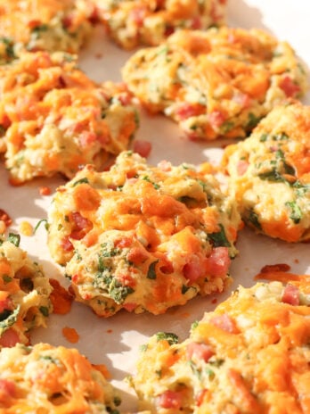 Cheddar biscuits with visible bits of ham and spinach, baked to a golden brown and arranged on a parchment-lined surface in bright natural light.