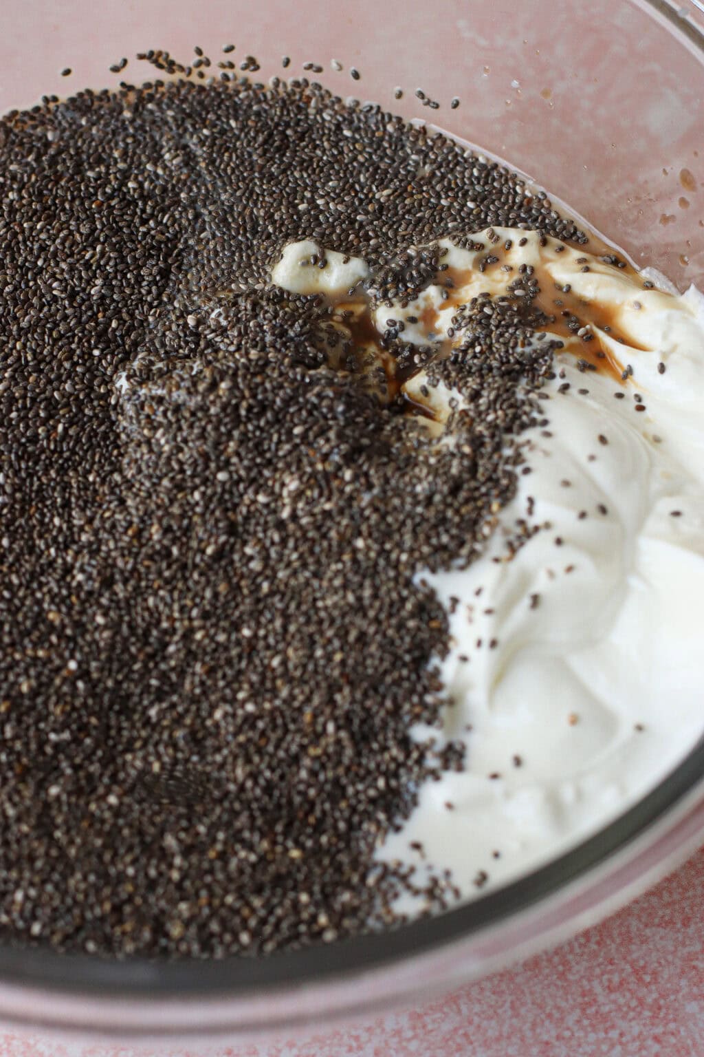 A close-up of a glass bowl filled with yogurt, chia seeds, and a drizzle of vanilla extract, ready to be mixed together.