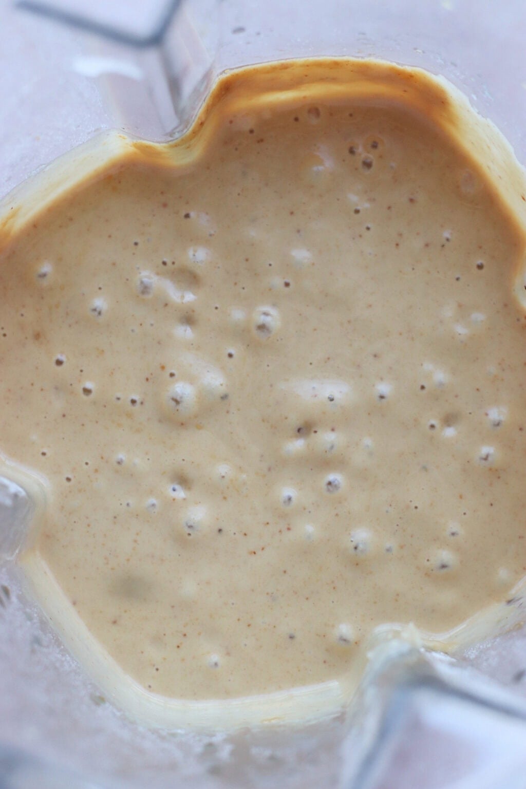 A close-up view of a creamy, light brown batter with small bubbles, seen inside a blender container.