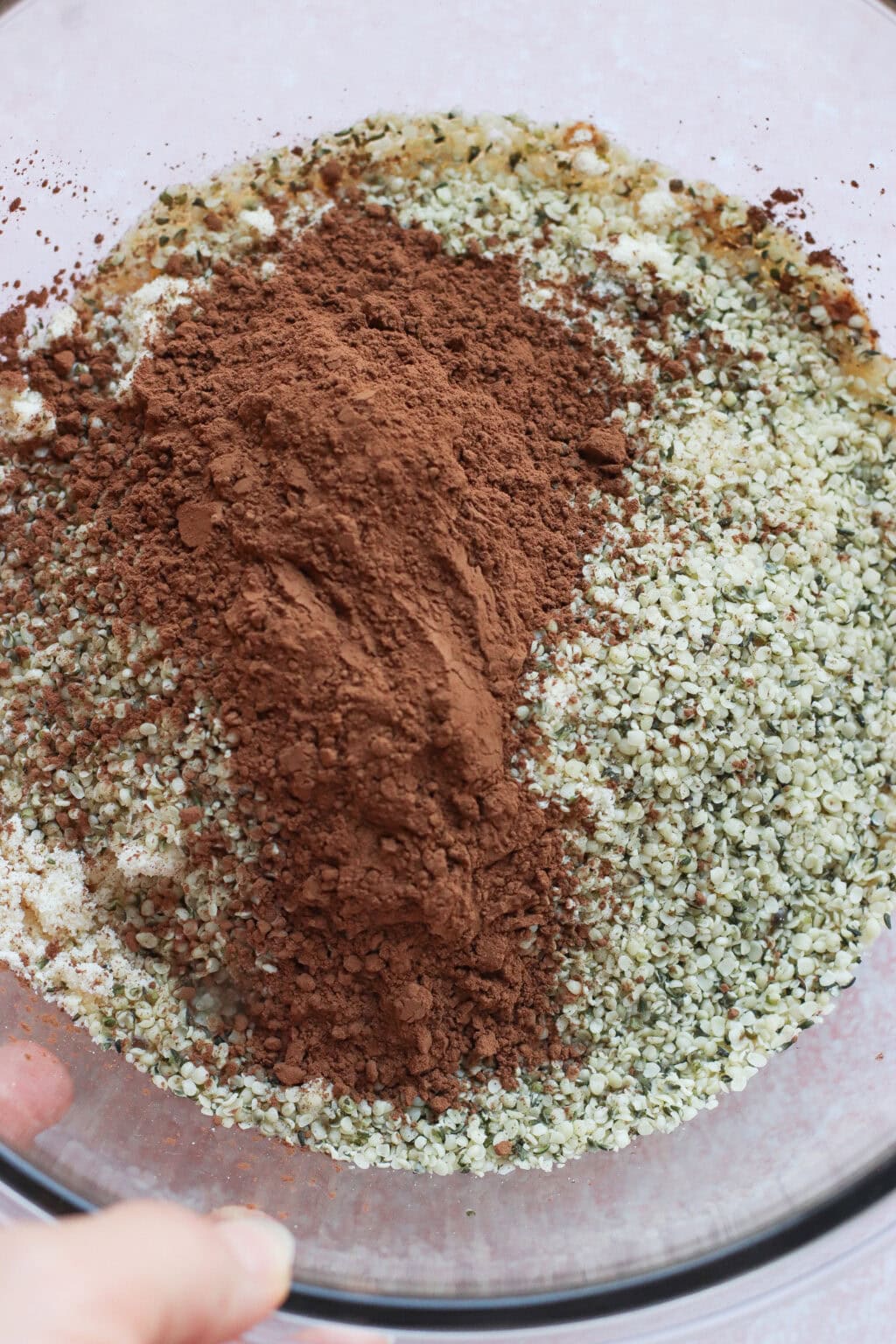 A glass bowl filled with a mixture of hemp seeds and a mound of cocoa powder, ready to be mixed for baking or cooking.