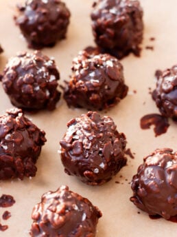 Chocolate-covered crunchy nut clusters arranged on parchment paper, with a glossy coating and a sprinkle of sea salt on top.