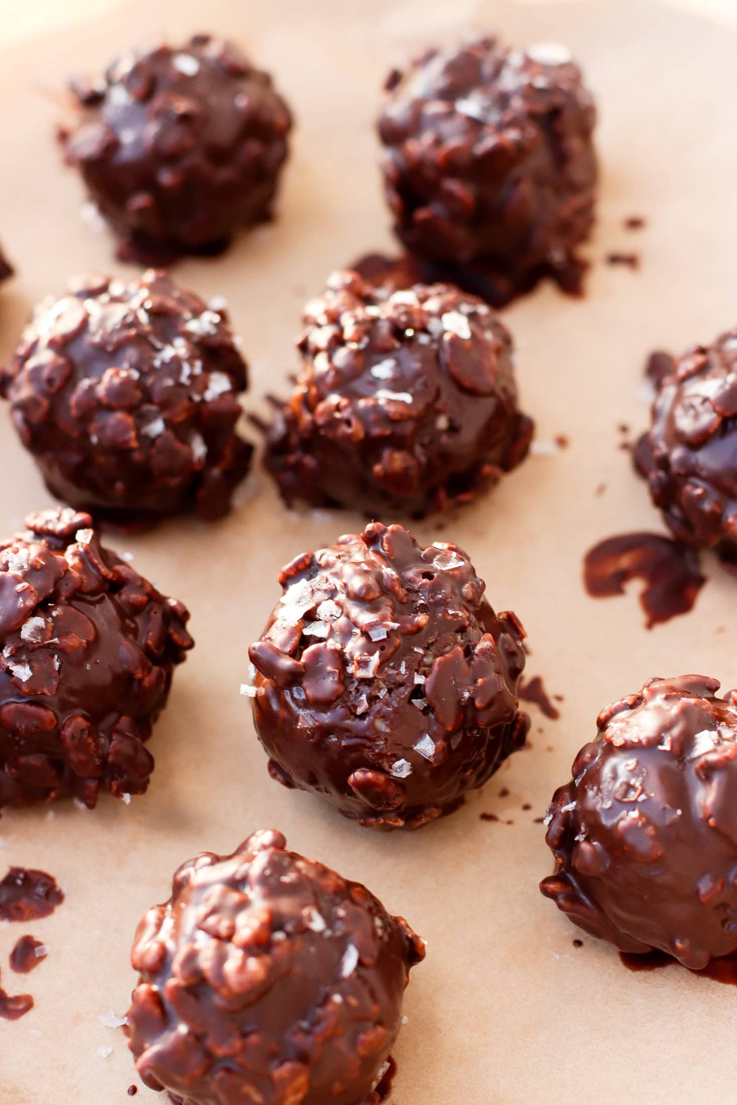 Chocolate-covered crunchy nut clusters arranged on parchment paper, with a glossy coating and a sprinkle of sea salt on top.