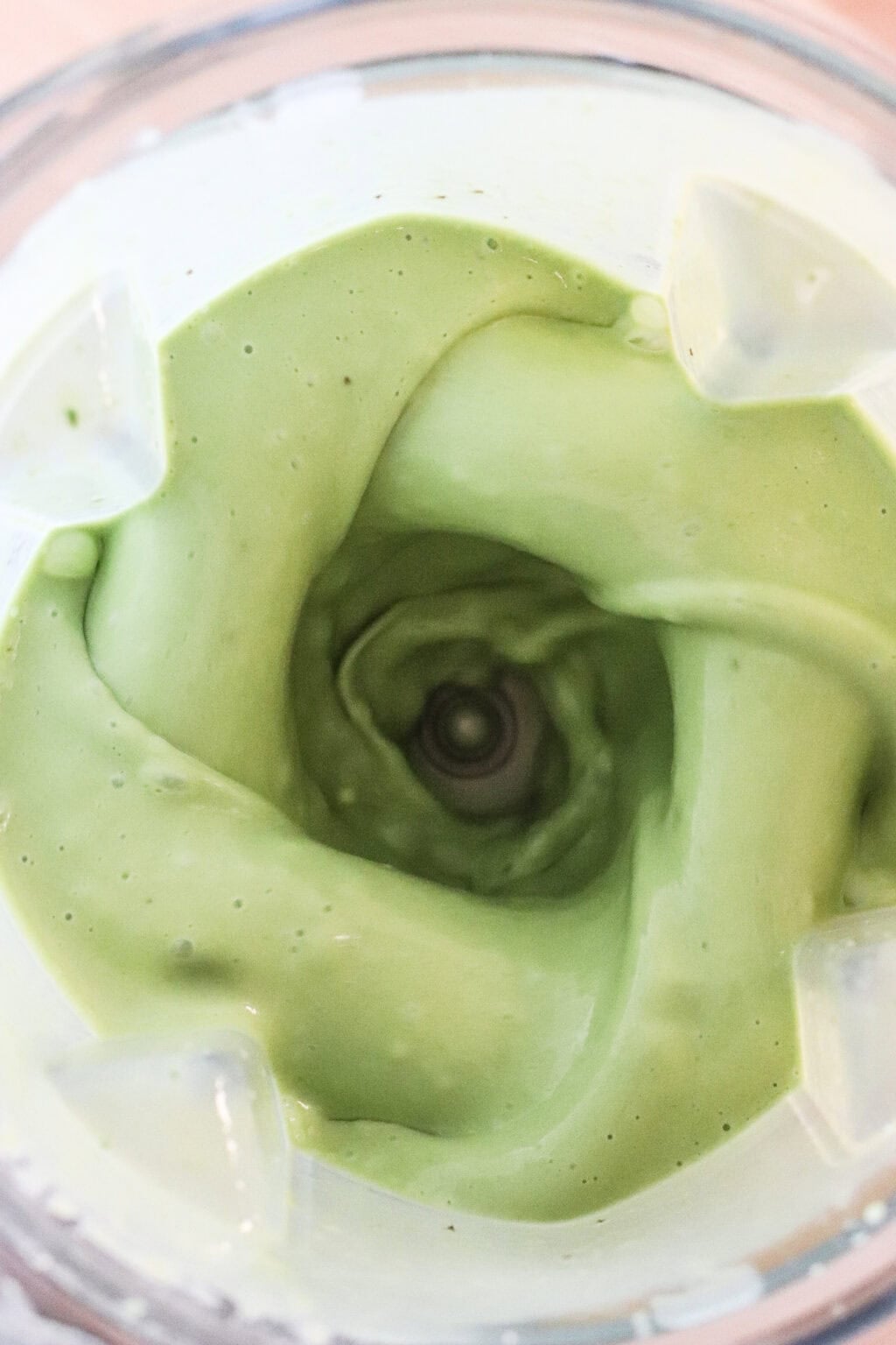 Close-up view of creamy green smoothie or sauce blending in a blender, showing a swirling vortex pattern at the center.